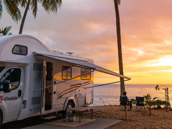 2 Reisende sitzen neben ihrem Wohnmobil mit ausgefahrener Schattenmarkise, während des Sonnenuntergangs an der australischen Küste/ Photo © CRUISIN Motorhomes 2 Reisende sitzen neben ihrem Wohnmobil mit ausgefahrener Schattenmarkise, während des Sonnenuntergangs an der australischen Küste
