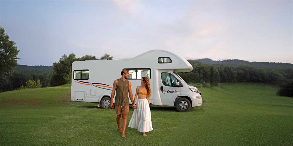 Zwei junge Menschen gehen über eine grüne Wiese auf ein Wohnmobil in Australien zu.