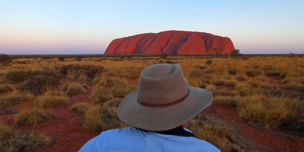 Ein Mann steht mit einem Hut vor dem Uluru in Australien