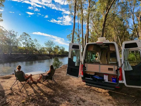 Zwei Menschen sitzen am Morgen, an einem Flusslauf in der aufgehenden Sonne vor ihrem Camper in Australien. Foto ©thl/maui Zwei Menschen sitzen am Morgen, an einem Flusslauf in der aufgehenden Sonne vor ihrem Camper in Australien.