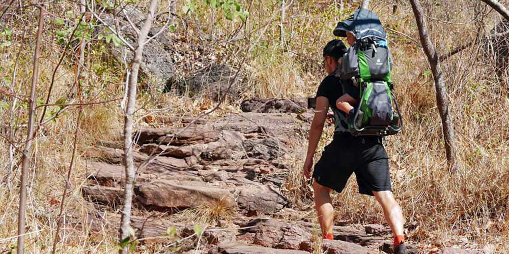 Ein Mann läuft mit einer Kindertrage einen Berg in Australien hoch.