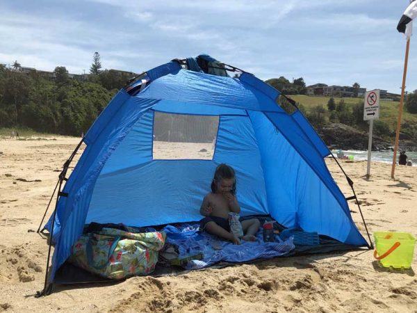 Ein Kind sitzt in einem Kuppelzelt an einem Strand in Australien / ©Photo: MietCamper Australien Ein Kind sitzt in einem blauen Schatten-Kuppelzelt an einem Strand in Australien