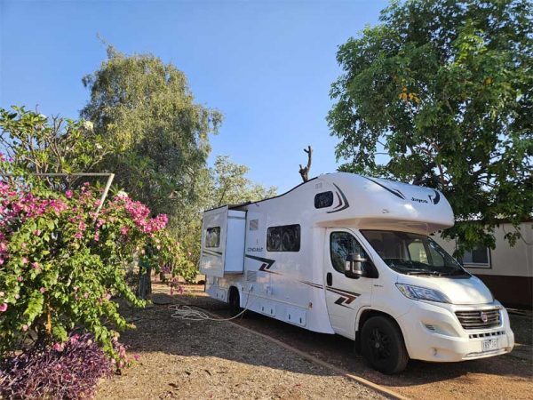 Ein Wohnmobil auf einem Campingplatz in Australien / ©Photo: MietCamper Australien Ein Wohnmobil steht auf einem Campingplatz in Australien, neben einem Busch mit rosaroten Blüten.