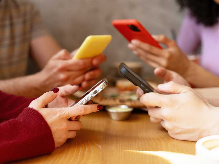 Hände von 4 Menschen bedienen ihre Smartphones, während sie um einen runden Tisch sitzen.
