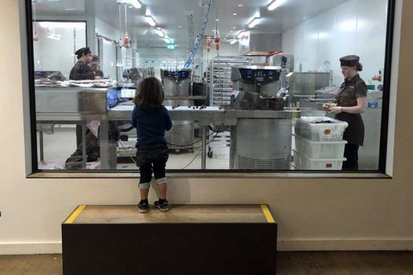 Ein Kind schaut durch eine Scheibe in die Produktion einer Schokoladenmanufaktur