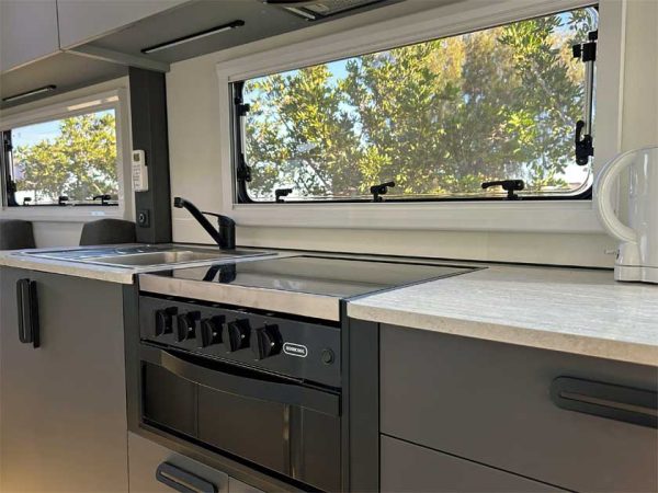 Eine Küchenzeile im Inneren eines australischen Wohnmobils mit Spüle, Kochfeld, Herd und Ofen. Darüber 2 Fenster die den Blick in die freie Natur zeigen./ Photo: © CRUISIN Motorhomes Eine Küchenzeile im Inneren eines australischen Wohnmobils mit Spüle, Kochfeld, Herd und Ofen. Darüber 2 Fenster die den Blick in die freie Natur zeigen.